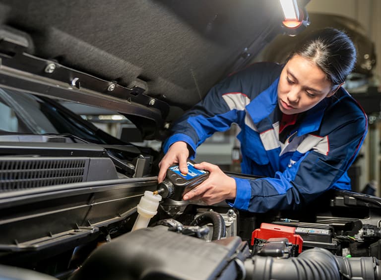 Eine Frau im blauen Arbeitsoverall füllt Motoröl von ECSTAR in einen Suzuki