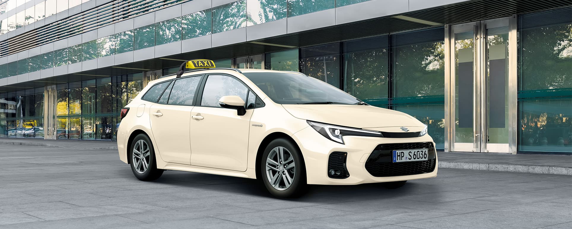 Ein Suzuki Swace in typischer Taxi-Optik mit hellgelber Lackierung und mit Taxi-Schild wartet vor einem Gebäude