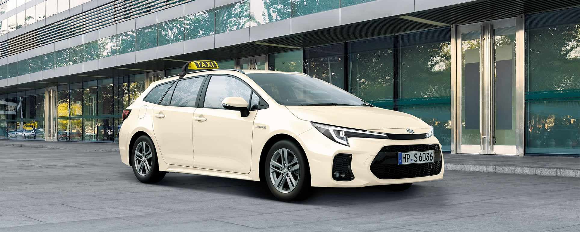 Ein Suzuki Swace in typischer Taxi-Optik mit hellgelber Lackierung und mit Taxi-Schild wartet vor einem Gebäude