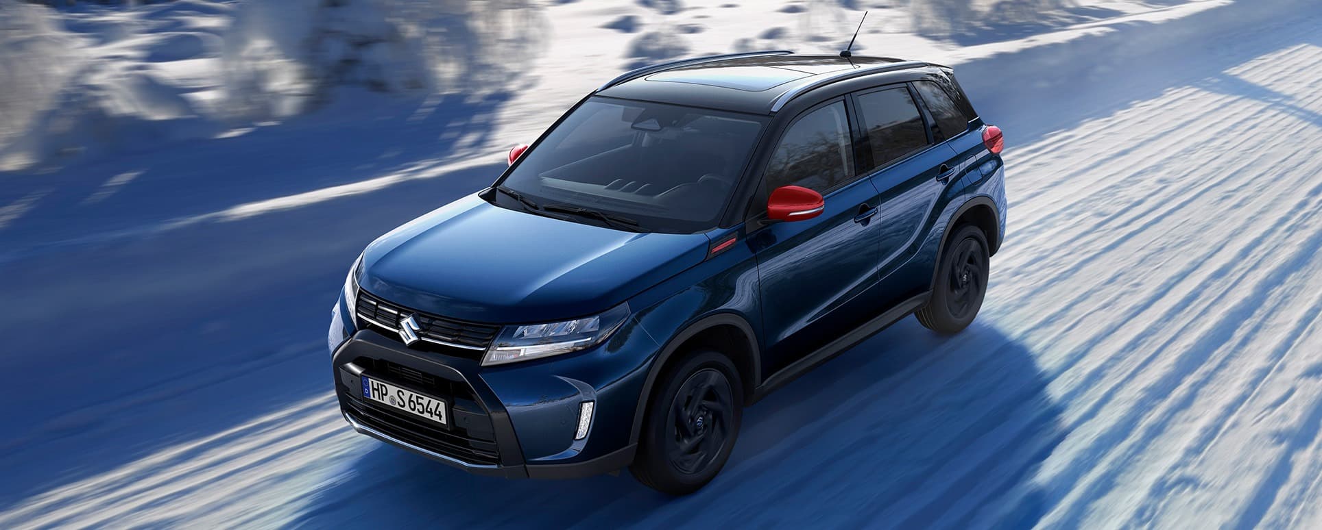 Abbildung zeigt dynamisch fahrenden, blauen Vitara auf einer schneebedeckten Landstraße