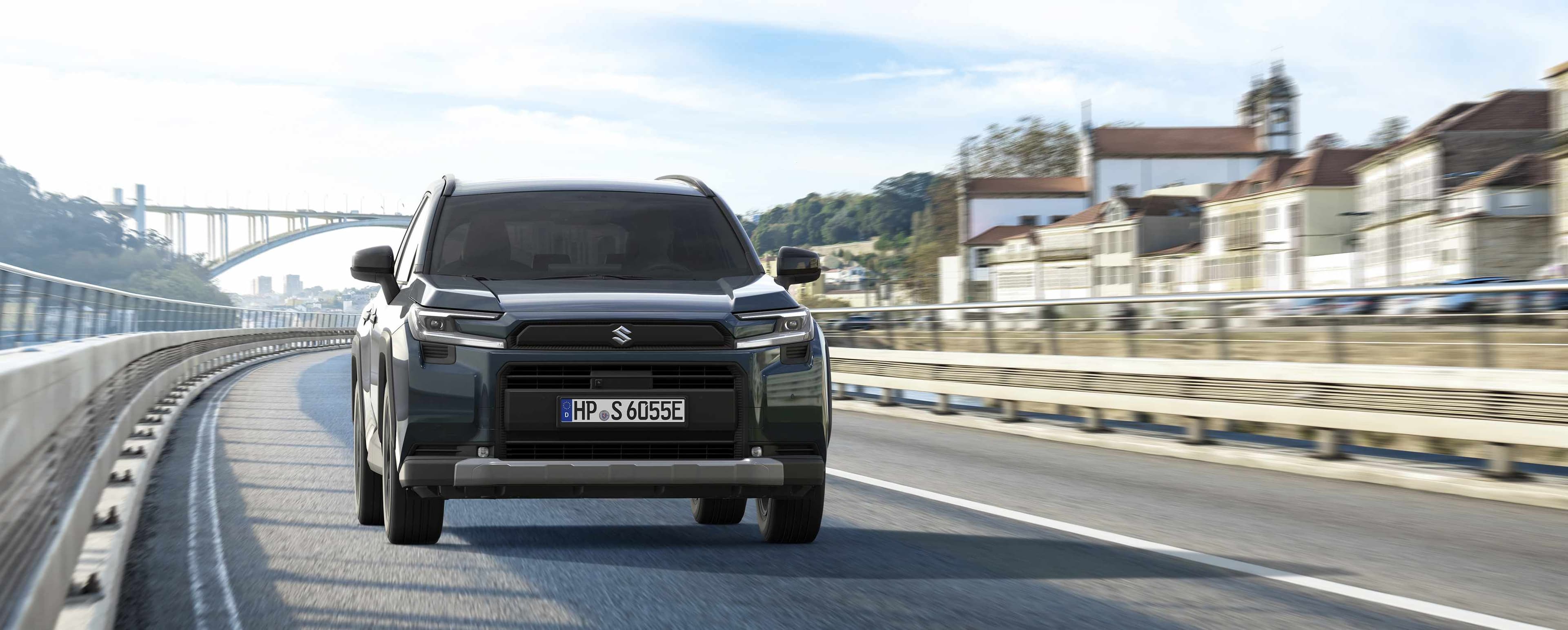 Ein dunkler Across 2.5 PLUG-IN HYBRID fährt auf einer Brücke in städtischer Umgebung auf den Betrachtenden zu.