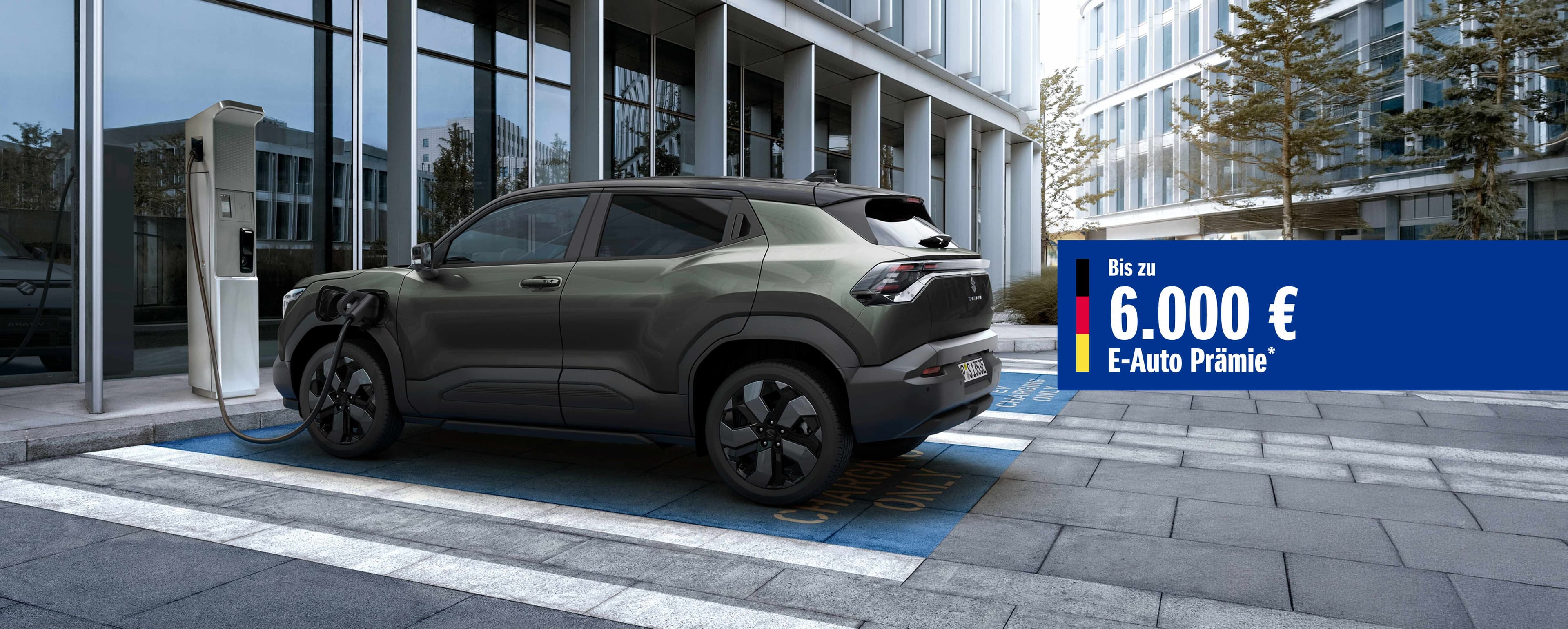 Dunkelgrüner Suzuki e VITARA parkt vor einem Gebäude mit Glasfront und wird geladen