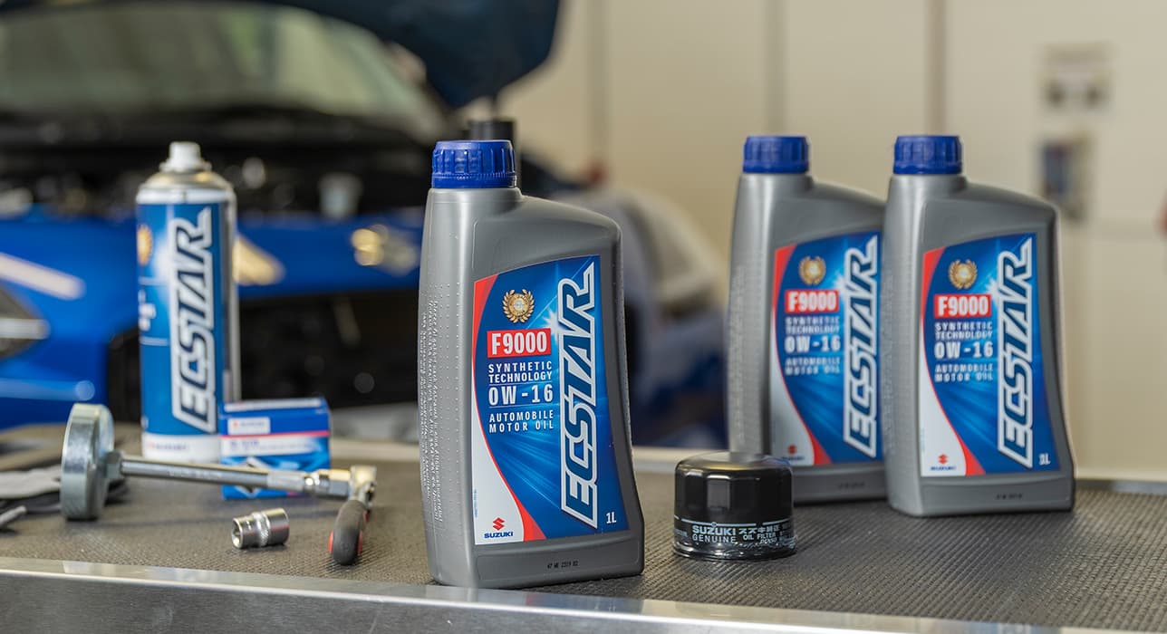 Eine Arbeitsoberfläche in einer Werkstatt, auf der mehrere ECSTAR Produkte stehen, im Hintergrund unscharf ein blauer Suzuki Swift mit geöffneter Motorhaube