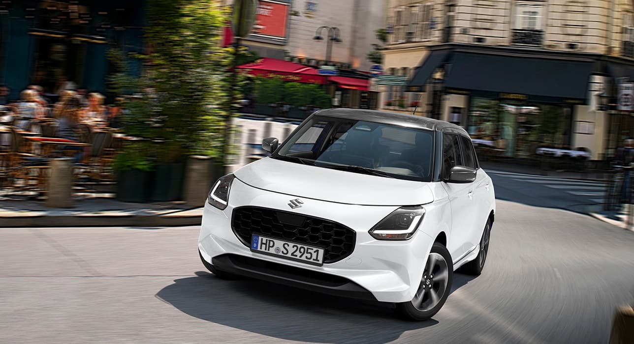 Ein weißer Suzuki Swift fährt in städtischer Umgebung dynamisch um eine Kurve