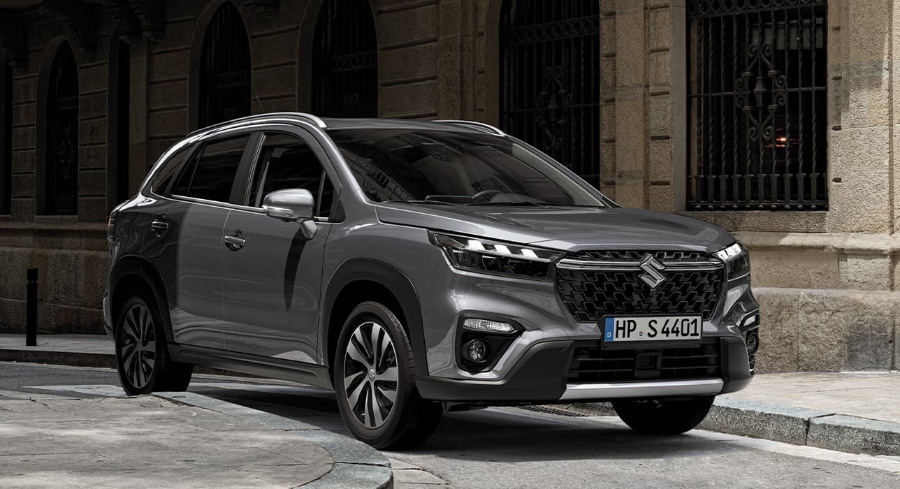 Abbildung zeigt einen S-Cross auf einer Straße vor einem Haus.