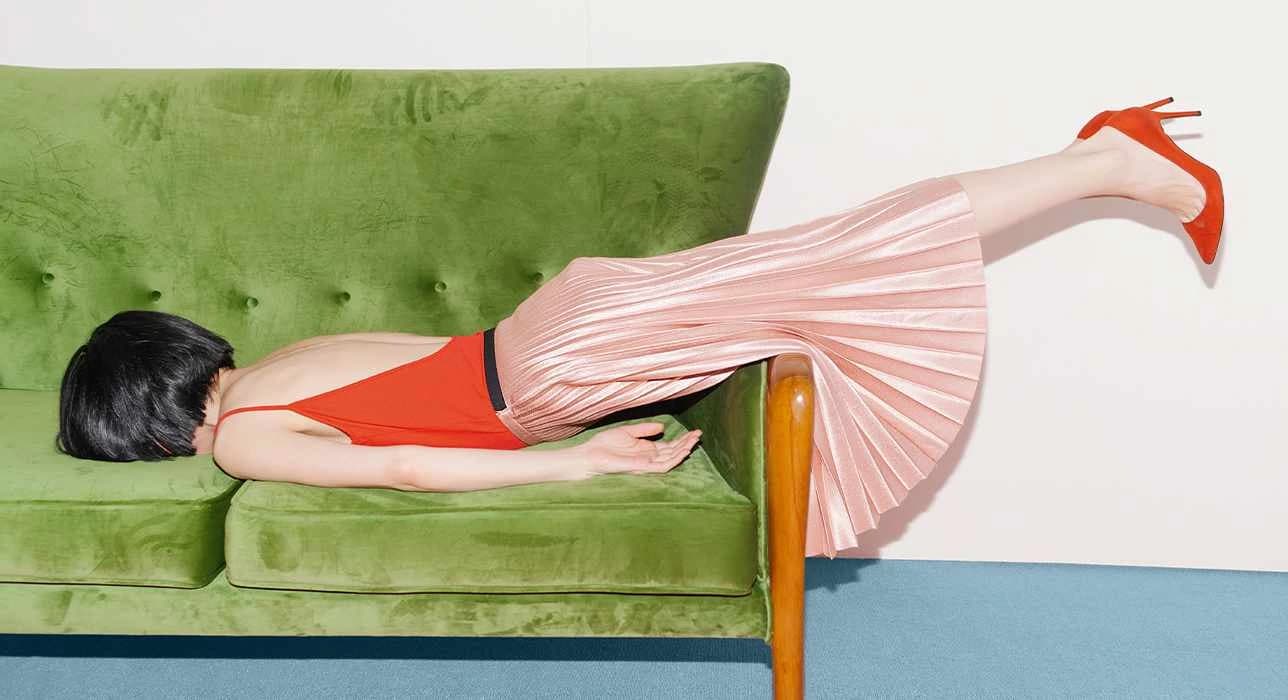 Frau liegt über die Armlehne gebeugt mit dem Gesicht auf dem Sofa