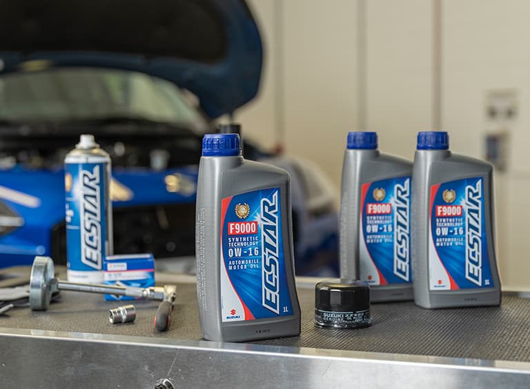 Eine Arbeitsoberfläche in einer Werkstatt, auf der mehrere ECSTAR Produkte stehen, im Hintergrund unscharf ein blauer Suzuki Swift mit geöffneter Motorhaube