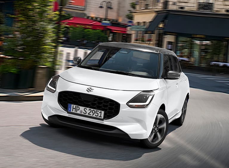 Ein weißer Suzuki Swift fährt in städtischer Umgebung dynamisch um eine Kurve