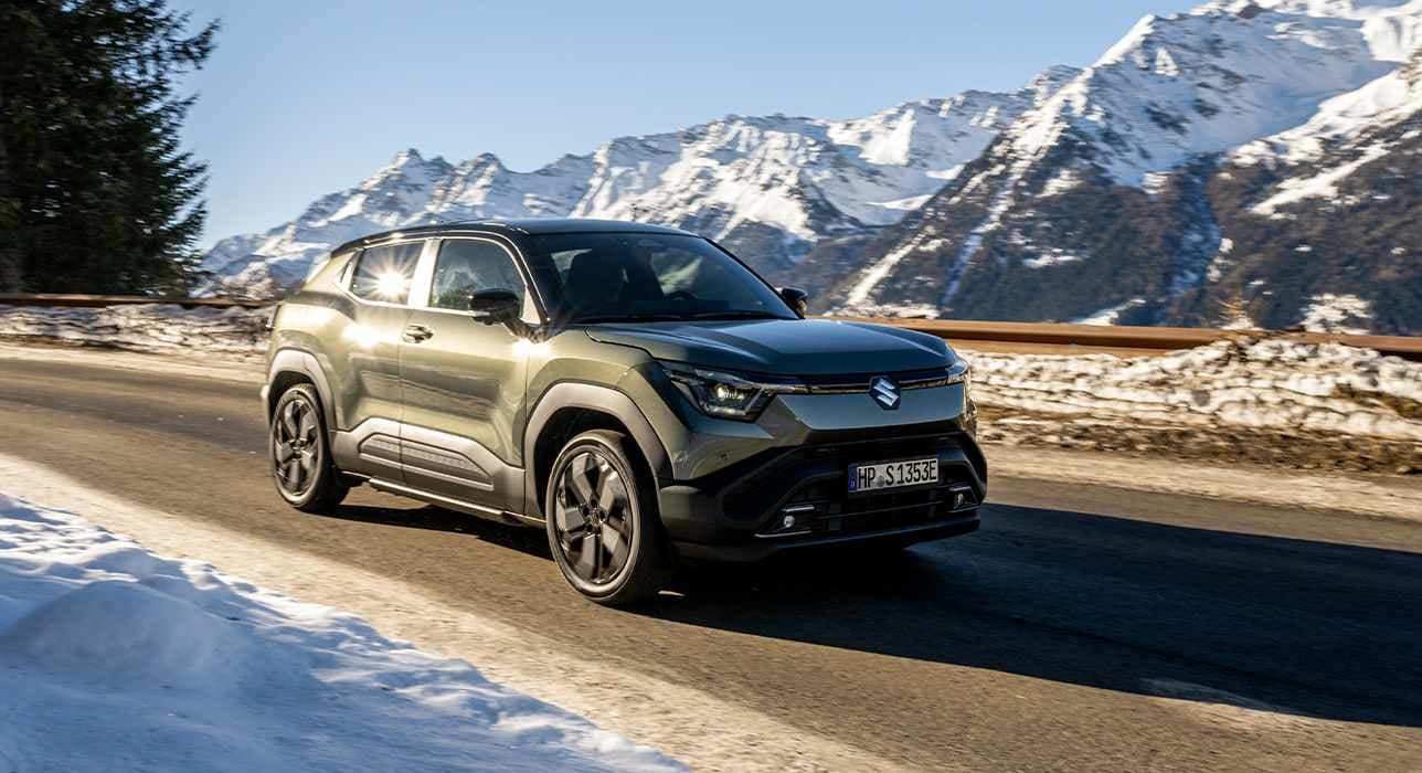 Suzuki e VITARA fährt auf einer Landstraße mit winterlicher und verschneiter Bergkulisse im Hintergrund.