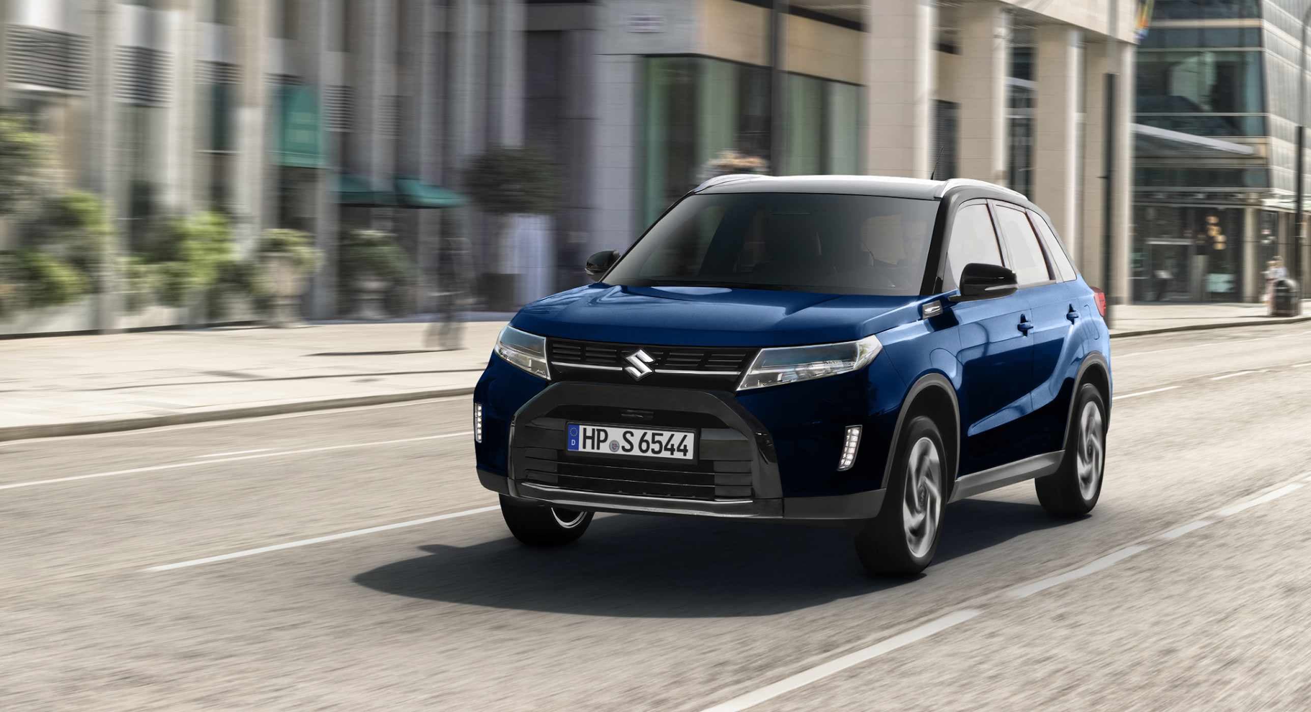 Dunkelblauer Suzuki Vitara Hybrid vor oranger Farbexplosion – Suzuki Deals, 5,3 l/100 km, CO₂ 120 g/km, Klasse D