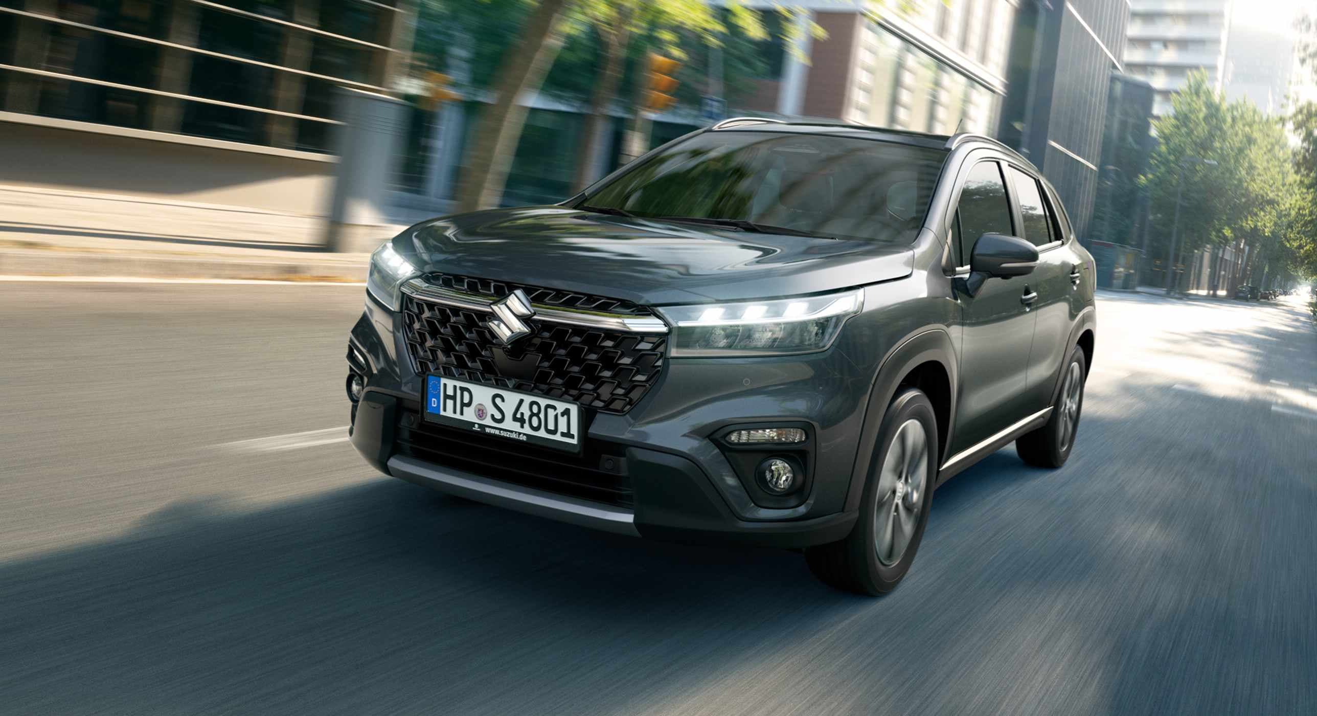 Abbildung zeigt einen grauen S-Croos auf einer Straße in einer Innenstadt