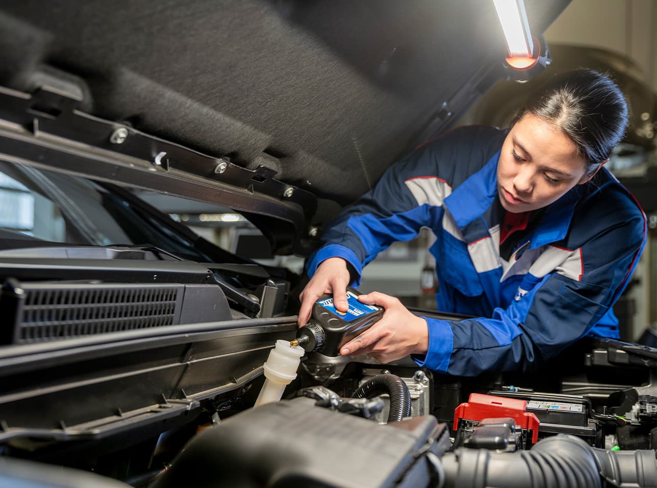 Eine Frau im blauen Arbeitsoverall füllt Motoröl von ECSTAR in einen Suzuki