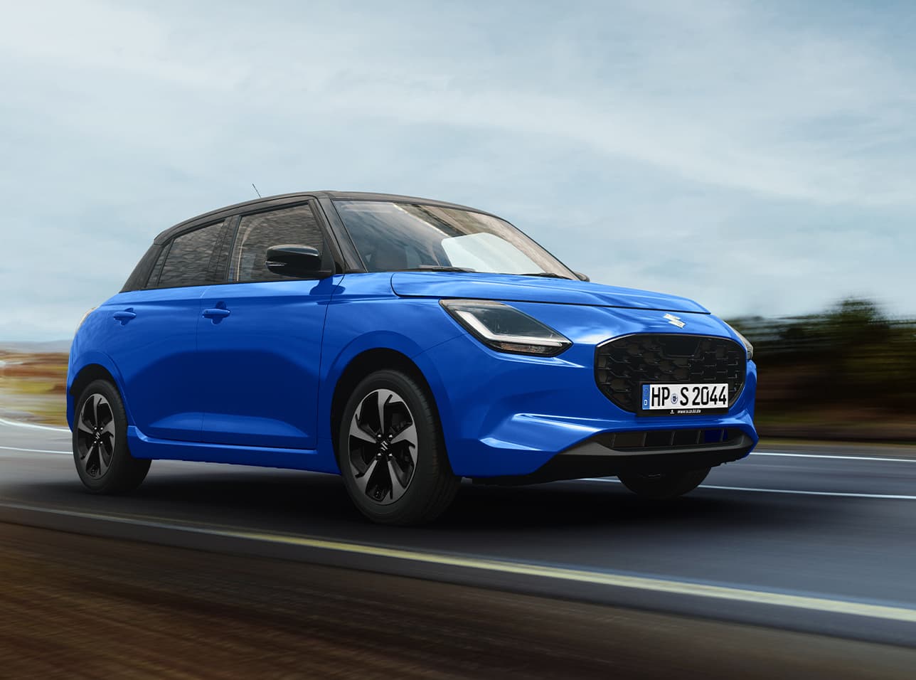 Ein blauer Suzuki Swift fährt dynamisch auf einer Landstraße