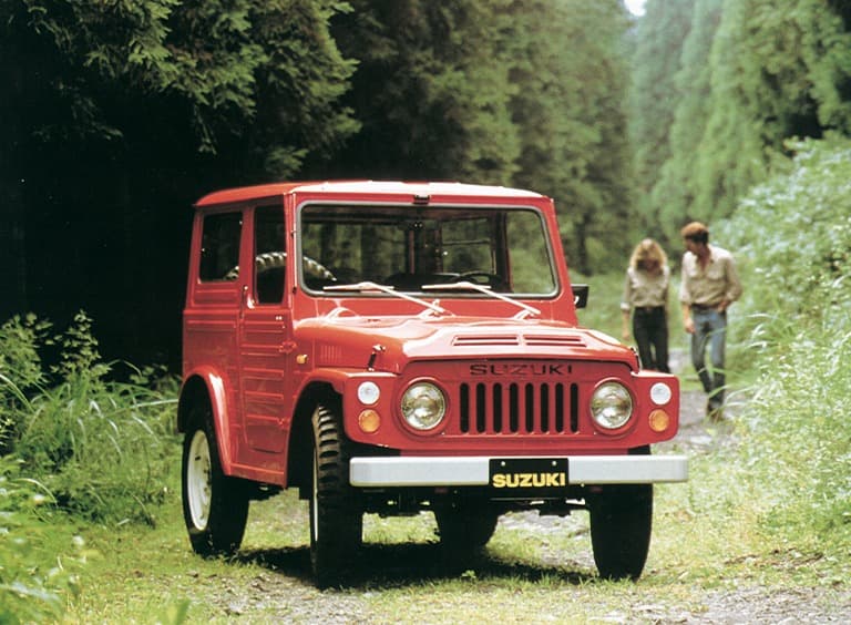 Abbildung zeigt einen roten Jimny parkend auf einem Waldweg