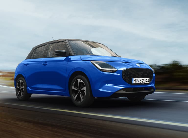 Ein blauer Suzuki Swift fährt dynamisch auf einer Landstraße