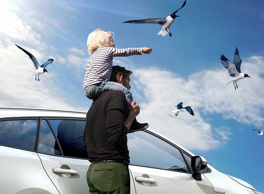 Mann steht mit Kind auf den Schultern vor Suzuki während Vögel am Himmel fliegen