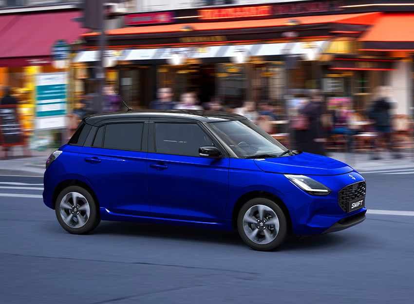 Blauer Suzuki Swift fährt dynamisch auf Straße