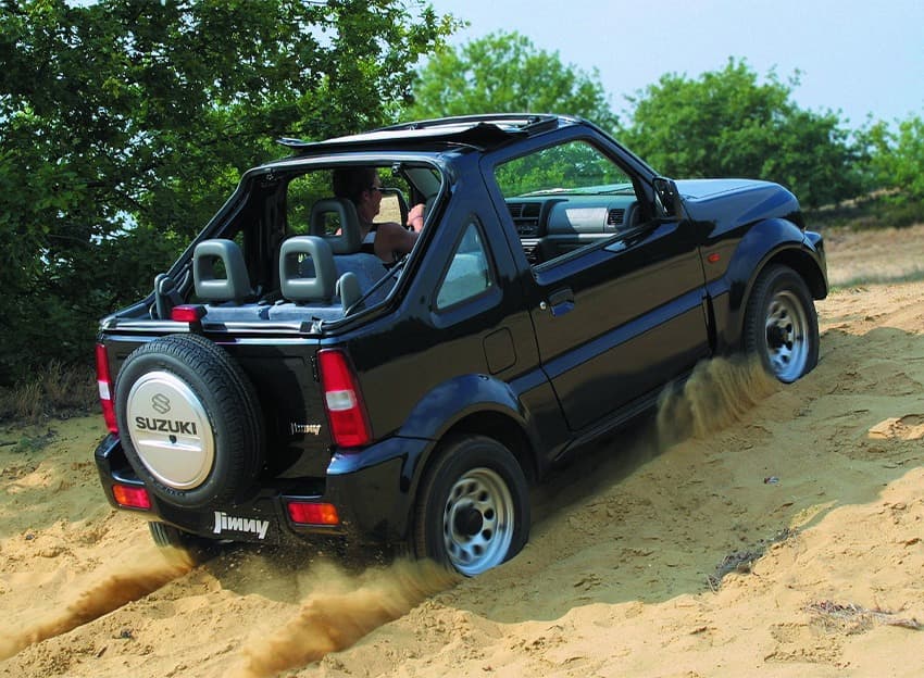 Abbildung zeigt einen schwarzen Jimny, der einen Sandhügel hinauffährt