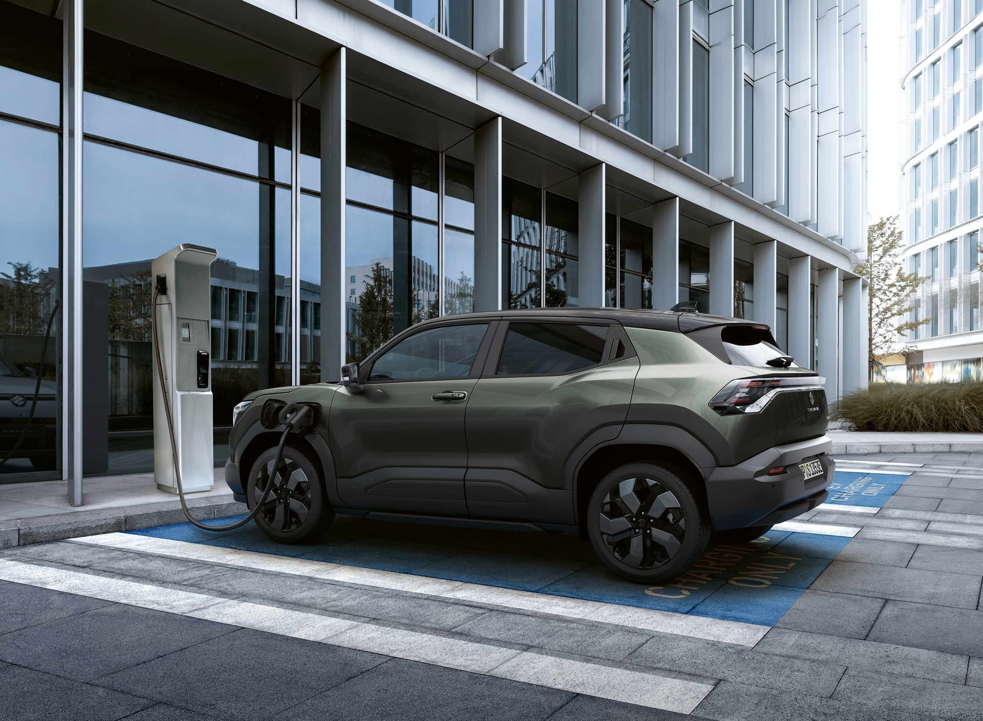 Dunkelgrüner e VITARA steht auf einem Parkplatz an einem Gebäude