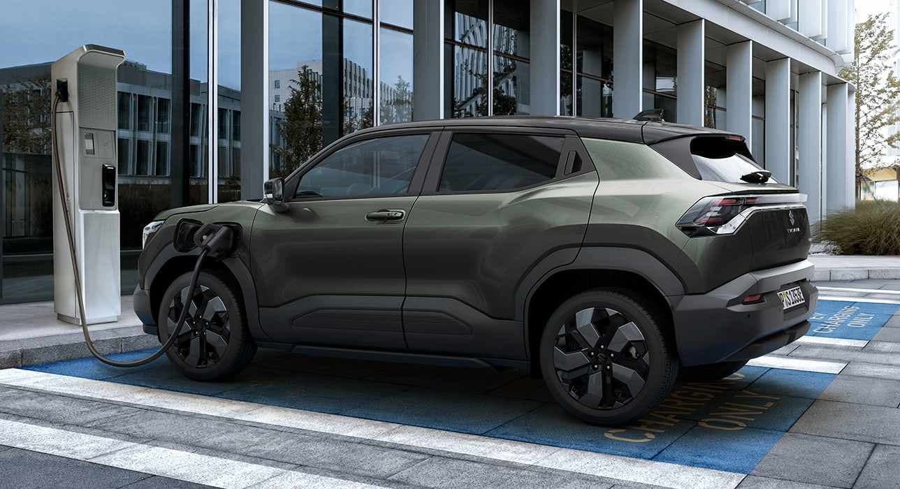 Der e VITARA in dunkelgrün lädt an einer E-Ladesäule.