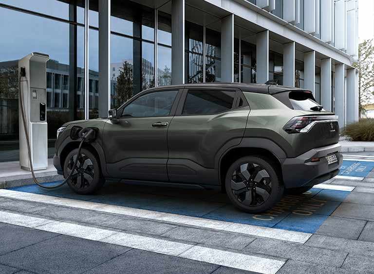 Der e VITARA in dunkelgrün lädt an einer E-Ladesäule.