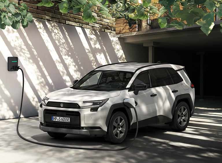 Ein heller Across steht im Halbschatten vor einem Carport, ein Ladekabel ist an einer Wallbox und der Ladebuchse des Autos angeschlossen.