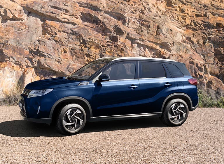 Abbildung zeigt blauen Vitara vor einem Hügel stehend