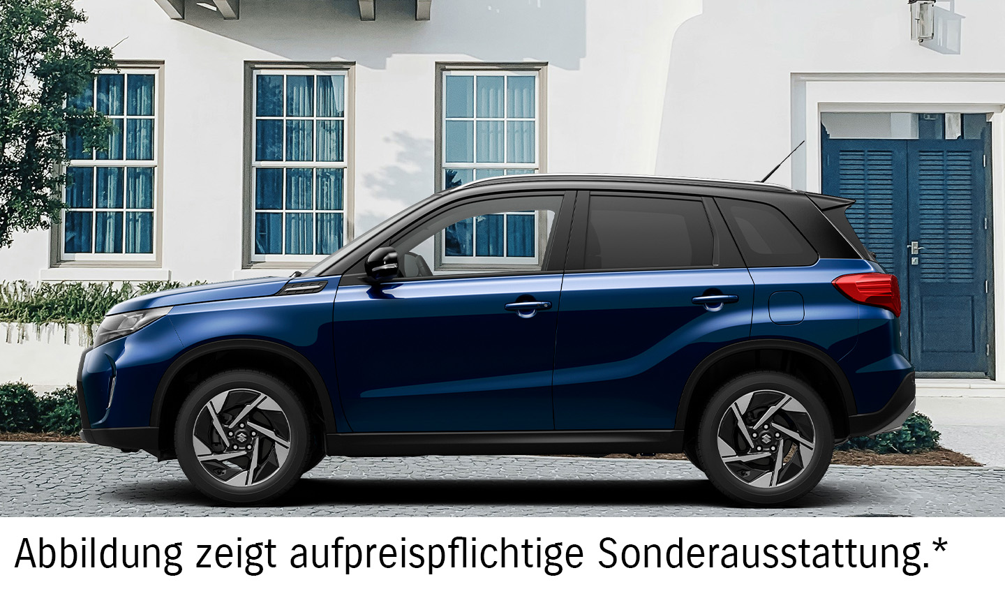 Dunkelblauer Suzuki Vitara in Seitenansicht vor einer hellen Hausfassade mit dunkelblauen Fensterläden und textlichem Hinweis auf die abgebildete aufpreispflichtige Sonderausstattung.