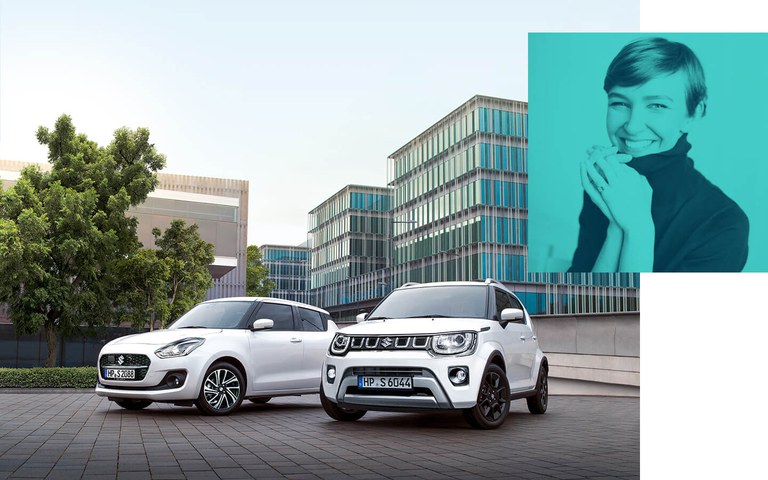 Ein Suzuki Swift Hybrid und ein Suzuki Ignis Hybrid  in Pure White Pearl Metallic, stehen vor einem Bürogebäude.