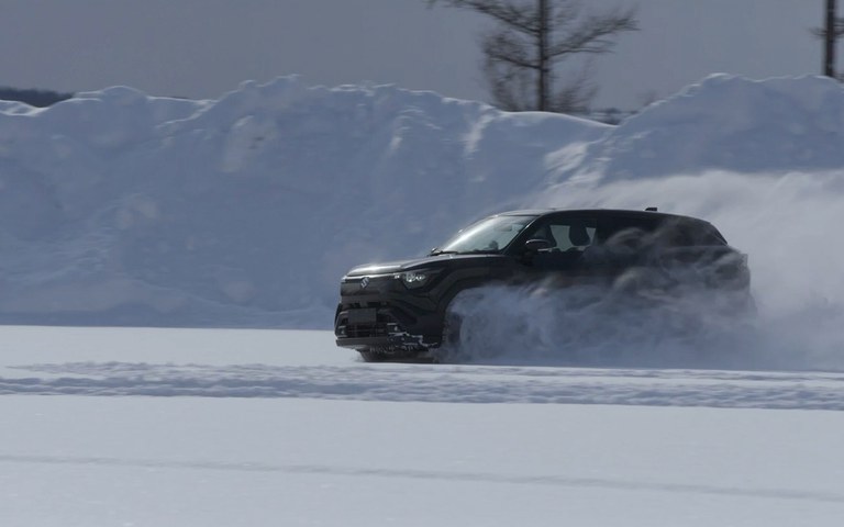 Grüner Suzuki e Vitara fährt auf schneebedeckter Straße durch Winterlandschaft