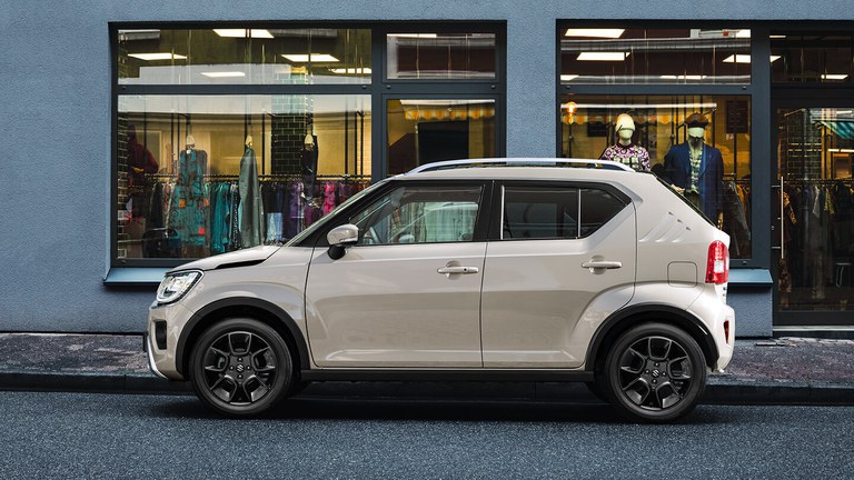 Suzuki Ignis Hybrid in Caravan Ivory Pearl Metallic parkt am Straßenrand vor einem Modegeschäft.