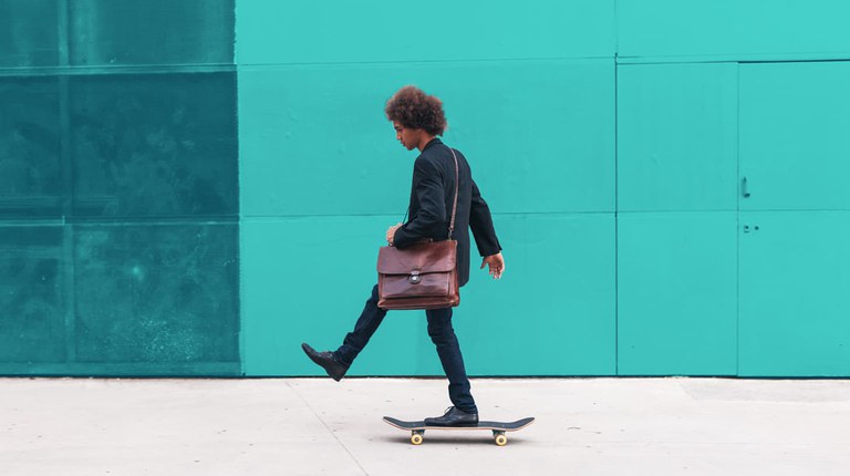 Ein junger Mann fährt auf einem Skateboard von rechts nach links. Vor dem Bild ist ein hellblauer Filter.