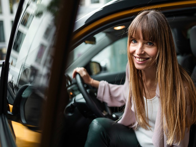 vitara-finanzierung.jpg Frau mit langen braunen Haaren steigt aus dem Suzuki Vitara Hybrid in Solar Yellow Pearl Metallic und grinst in die Kamera.